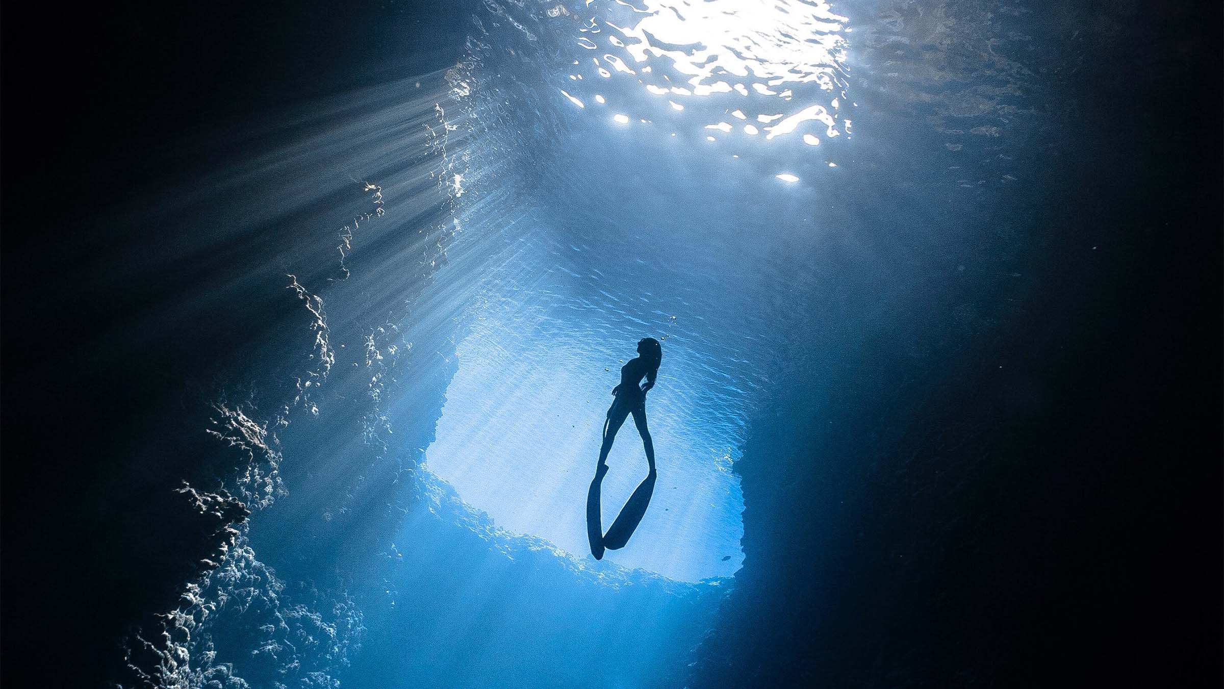 Woman swimming underwater towards bright light